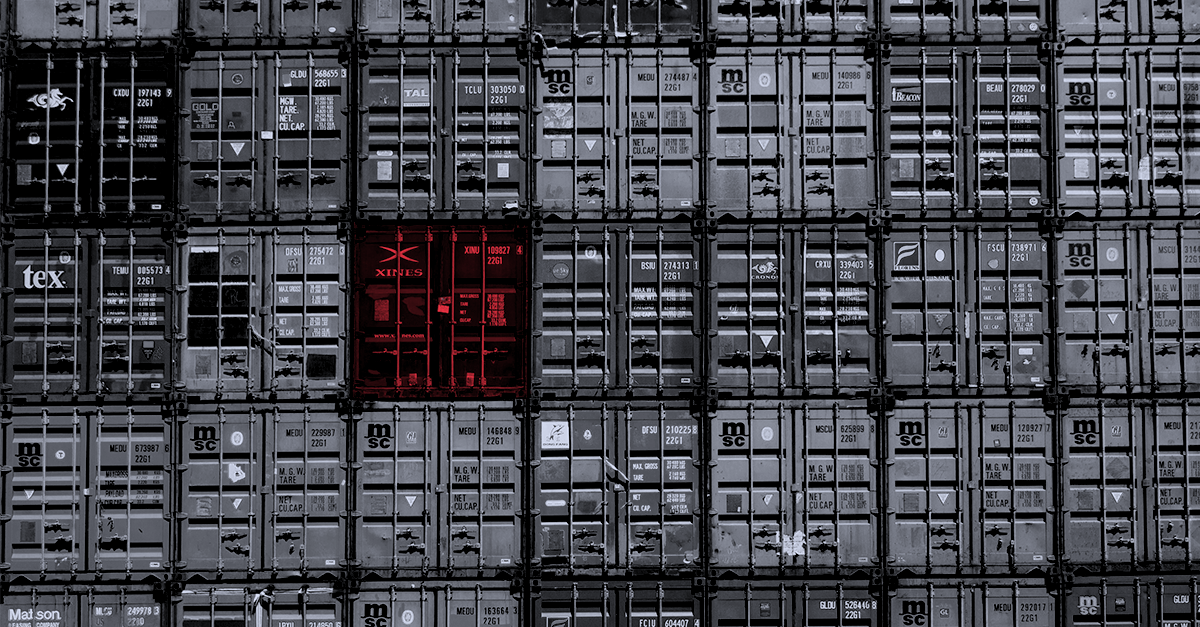Stacked shipping containers with one highlighted in red, symbolizing transshipment risks and global supply chain vulnerabilities.