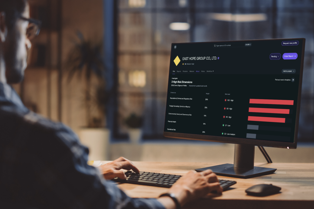 Person reviewing a company risk profile in the Exiger Knowledge Graph platform on a desktop computer, showing an assessment for East Hope Group Co., Ltd. with visualized risk levels across multiple dimensions including reputational, foreign ownership, and operational risk.